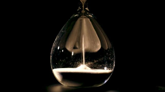 Close-up of hourglass with falling sand on black background