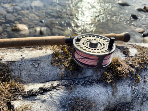 Fly fishing rod and reel gear equipment on dead tree with river in background during summer time sun rise on water