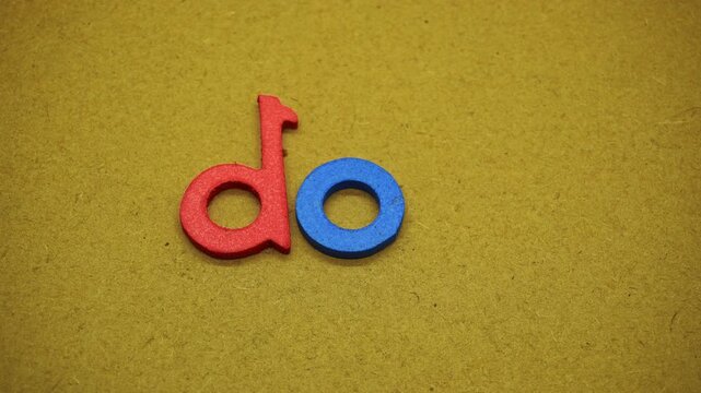 Hand arranging colorful alphabet letters spelling do it on brown craft paper background top view representing proactive action execution motivation and determination