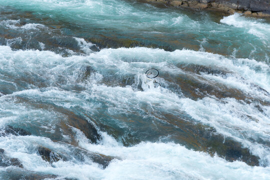 Canada, Alberta, Banff.  Turbulent waters flow over an abandoned bicycle in the Bow River Falls.