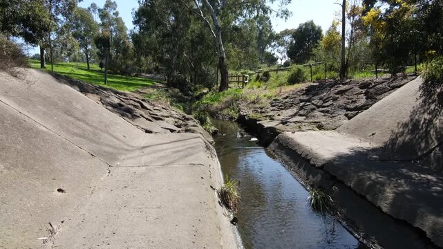 Concrete stormwater canal of Stony Creek, with&nbsp;sloped concrete embankments, basalt rock retaining walls. Urban water channel&nbsp;in Melbourne, Victoria, Australia