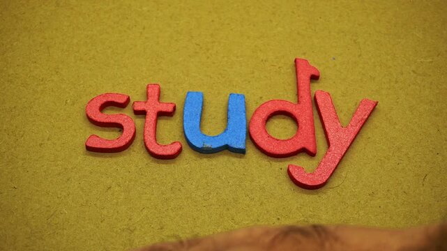 Male hand removing colorful wooden letters spelling study on textured surface, illustrating concept of stopping learning, school burnout, study break, or exam completion.