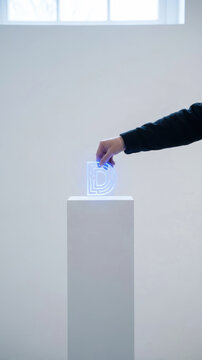 Minimalist data driven decision making concept with hand placing glowing digital symbol on white pedestal in modern gallery
