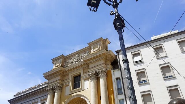 Tilt-down view from an ornate cast-iron streetlamp to San Pietro Apostolo&rsquo;s Neoclassical facade in Piazza Garibaldi, Parma, beneath a clear blue sky.