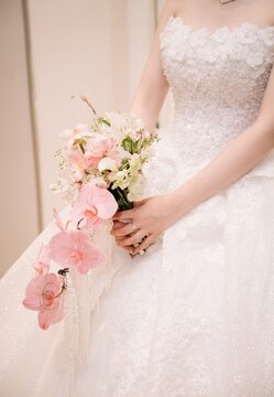 A bride in an ornate white lace wedding gown holding a cascading bouquet of pink orchids and white flowers.