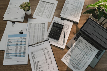 Financial reports, calculator, laptop and accounting documents arranged on office desk for...