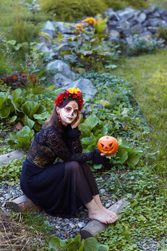 Halloween portrait of female sitting on a wooden staircase in garden with Halloween pumpkin in hand.