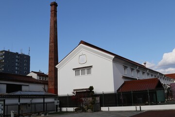Traditional Japanese sake brewery with a historic brick chimney under a clear blue sky, Saijo, Hiroshima. © Arai