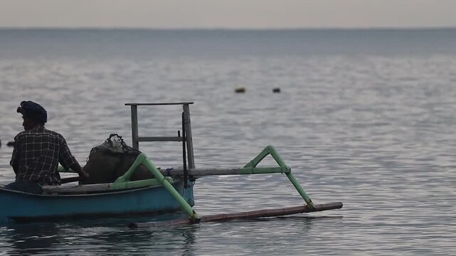 Fisherman Rowing Traditional Blue Jukung Boat on Calm Sea at Teluk Waru Sekotong Lombok