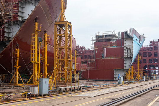 Large steel hull block surrounded by shipyard infrastructure and construction equipment, representing modern industrial shipbuilding and prefabrication techniques.