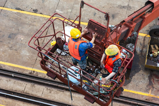 Two shipyard workers in a lifting platform carrying out maintenance and finishing work on the side of a newly built vessel.