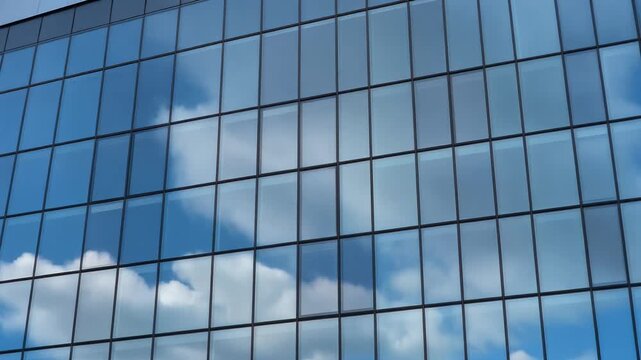 Modern office building glass facade reflecting a bright blue sky with white clouds in an abstract architectural pattern