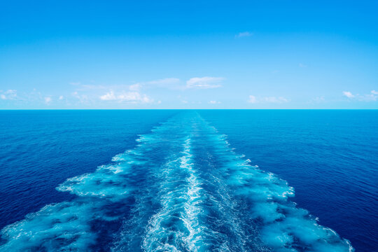 Water wake trail left by cruise ship in deep blue ocean under clear sky with copy space