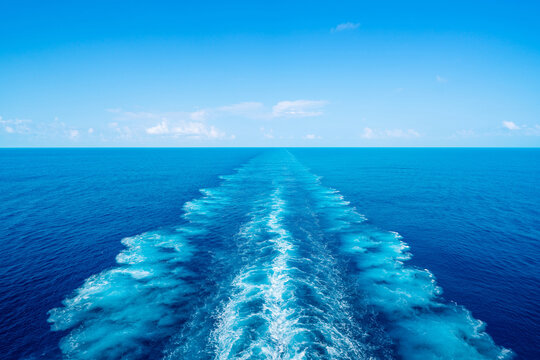 Water wake trail left by cruise ship in deep blue ocean under clear sky with copy space