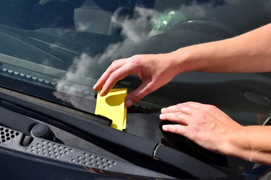 A yellow fine notice under the car's windshield wiper. A parking fine notification. The vehicle is parked in a prohibited area, or the parking time has expired.