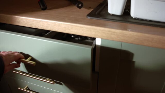 Hand closes kitchen drawer of utensils slow motion medium zoom shot selective focus