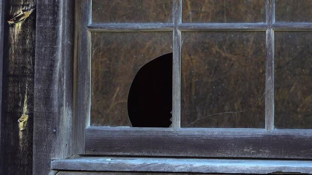 A detailed macro shot focuses on a clean hole in a glass window pane set against aged wood and abstract reflections.