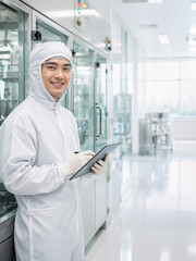 Fototapeta premium Scientist smiling while documenting on clipboard in sterile cleanroom, representing pharmaceutical research.