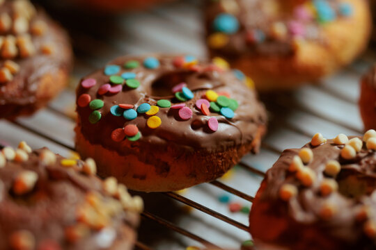 Close Up View Of Homemade Healthy Chocolate Glazed Doughnut With Colorful Sprinkles. Appetizing macro shot showcasing sweet nutritious pastries cooling on a metal grid