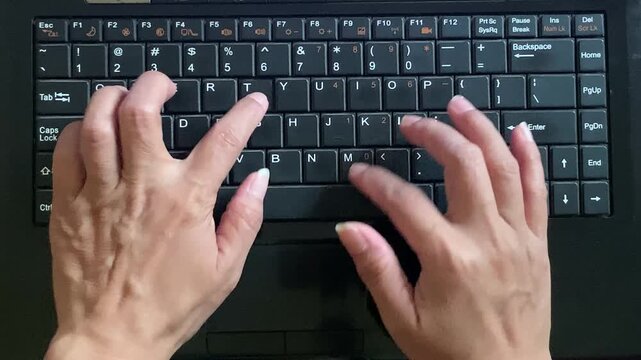 High-angle top view of a user's hands typing quickly on a black laptop computer keyboard. Excellent commercial stock photo for business productivity, software development, and online work.