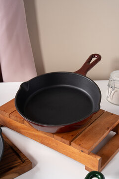 Empty red enamel cast iron skillet pan placed on wooden trivet stand on white table