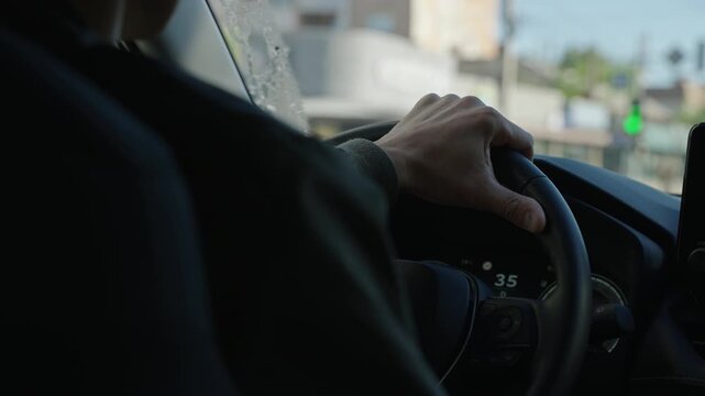 Close-up shot of a male hand on a wheel of a new car driving with a speedometer on the background and the city streets going past.