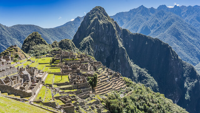 Panoramic landscape of the ancient famous Machu Picchu. There are masonry buildings, terraces, and stairs on the hillside. Huayna Picchu, a mountain range of the Andes against a blue sky. Peru. Cusco.