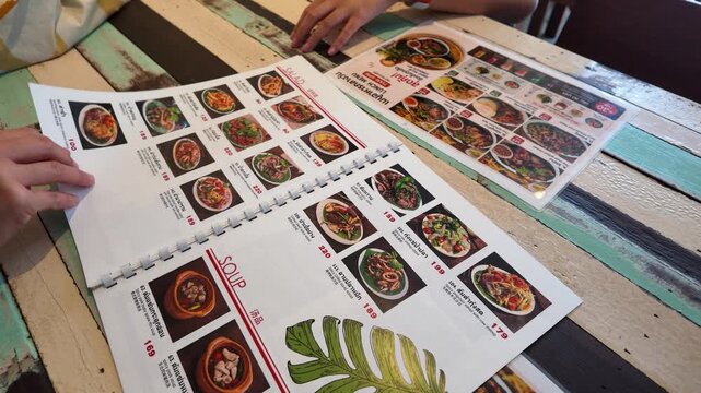 Hands Flipping Through Asian Food Menu at Wooden Restaurant Table