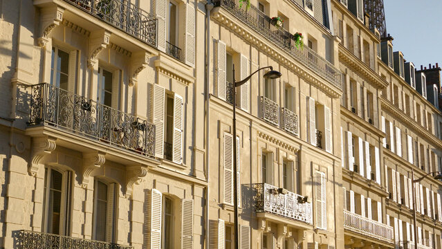 Haussmann style building facade with many balconies and closed shutters under sunlight