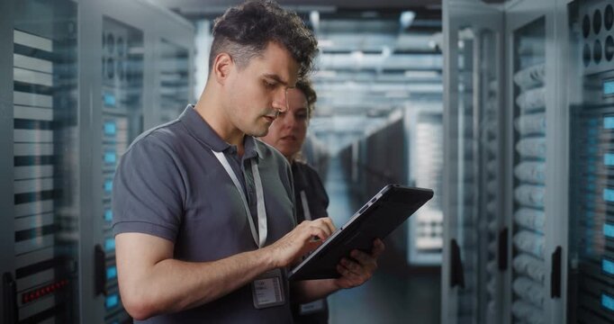 Professional IT Specialist Operates Tablet Computer to Monitor System Status while Female Colleague Inspects Server Rack Hardware. Team Collaboration Ensures Smooth Cloud Infrastructure Performance.