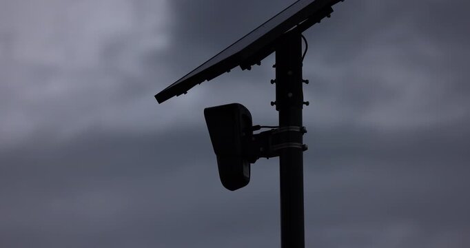 Ominous storm cloudy view of an AI artificial intelligence camera and solar panel on a pole.