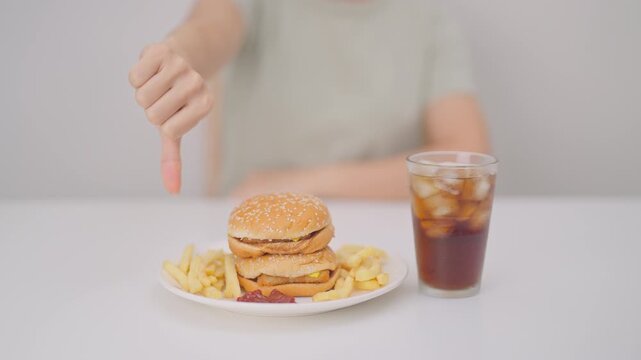 woman showing thumbs down, Rejecting and refusing with Juicy beef burger, potato chips and carbonated Soft drinks. Unhealthy, High calorie, Fast food craving, Obesity, diet, weight loss and junk food