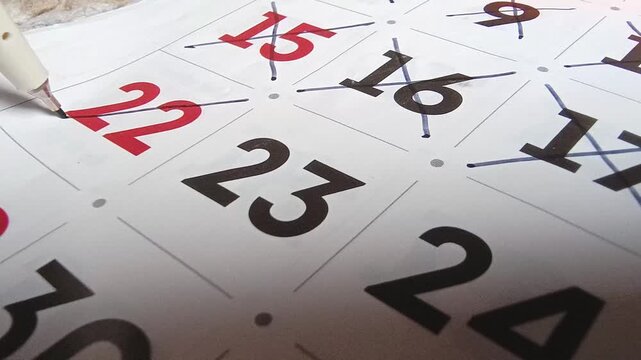 Close up view of person marking off dates on paper calendar with pen, time management and scheduling concept