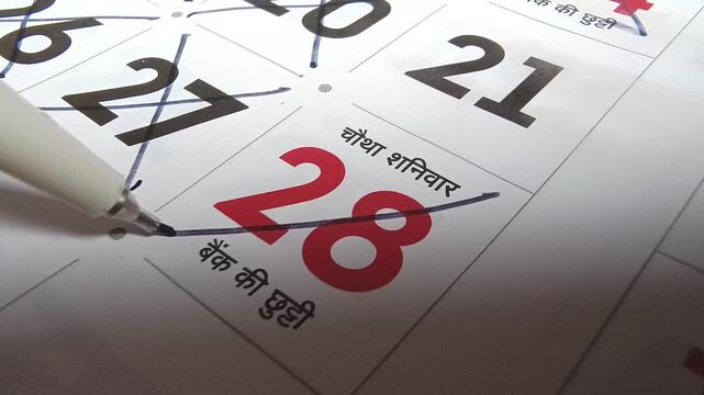Close up view of person marking off dates on paper calendar with pen, time management and scheduling concept