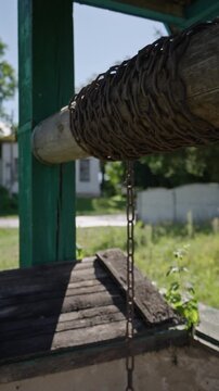 Vertical wide angle of a pulley well system with an axel and a chain on it. The axel of the pulley well rotating back and forth. Ascending and descending well pulley chain.