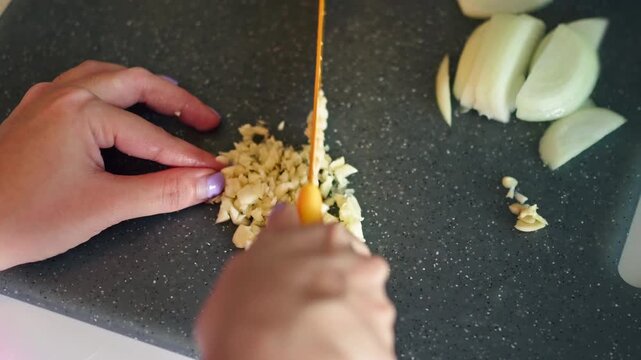 Top view of a woman preparing ingredients and chopping garlic in the kitchen, cooking at home, fresh food preparation, healthy lifestyle, and culinary activity concept.
