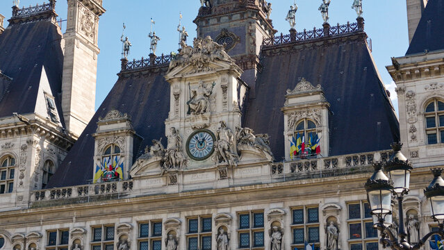 Hotel de Ville facade with clock, statues, and flags under a clear blue sky