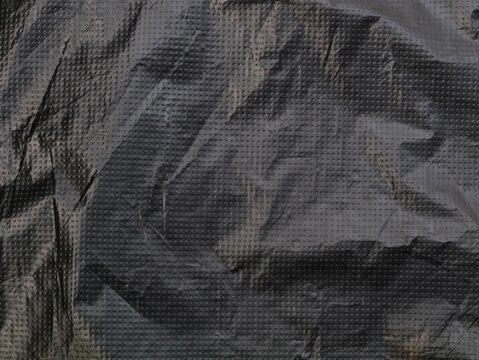 Close up of a dark gray crumpled plastic tarp texture with dotted grid pattern. Ideal for abstract industrial backgrounds, waterproof fabric surfaces, synthetic material designs, and dark cover macro