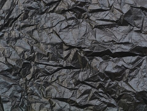 High detail background of a heavily crumpled dark plastic material with a micro-dotted grid pattern. Ideal for abstract industrial overlays, moody dark backdrops, and modern synthetic textures