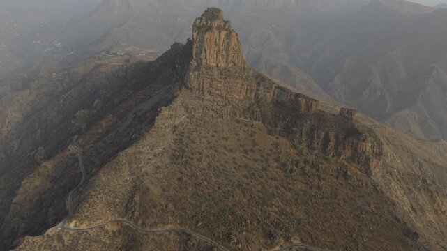 Aerial drone flying backwards revealing the stunning Roque Bentayga monolith. Rugged, arid terrain in Gran Canaria, Canary Islands, Spain