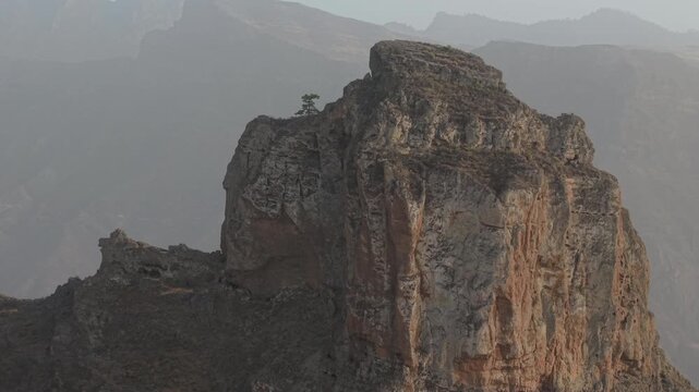 Striking aerial view showing the imposing Roque Bentayga in Gran Canaria during a hazy sunset, revealing its rugged volcanic texture
