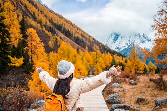 Young female tourist relaxing and enjoying at beautiful autumn scenery landscape at Mount Siguniang national park in Sichuan, China