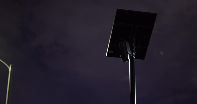 Night view of an AI artificial intelligence camera and solar panel on a pole at night with clouds behind.