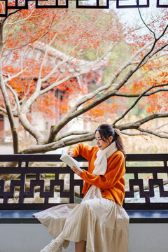 Peaceful autumn moment, A young woman sitting by a traditional Chinese carved window with colorful fall foliage.