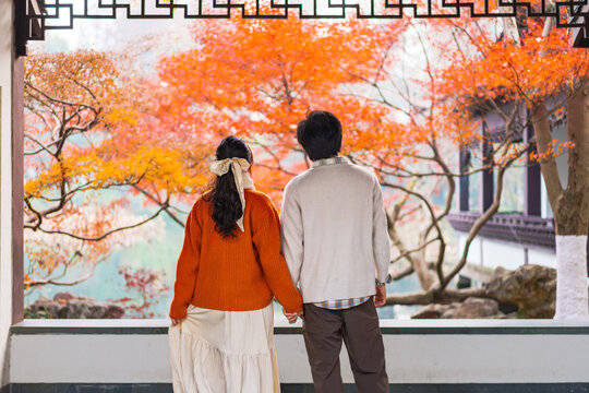 Young couple looking through a traditional Chinese carved window with colorful fall foliage, Peaceful autumn moment
