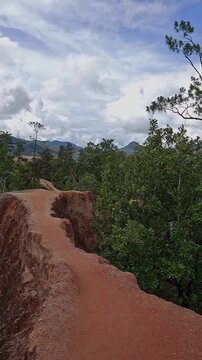 Red laterite soil erosion gully cutting through tropical forest with distant mountains under dramatic cloudy sky, Pai Canyon, Thailand