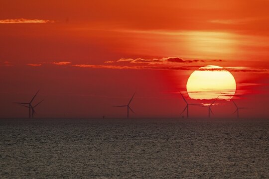 Dramatic sunset over the sea, wind turbines and wind turbines on the horizon, streaks of clouds, Houvig Beach, North Sea, Denmark