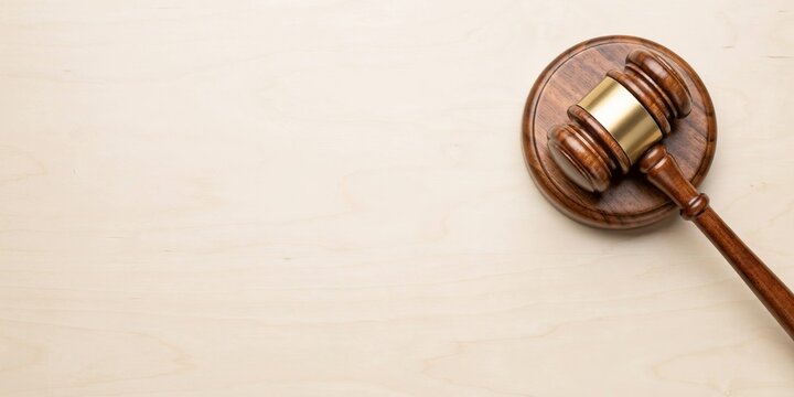 A wooden judge gavel resting on a matching round wooden sound block, positioned on the right side of a light wooden surface, symbolizing law, justice, court, and legal authority with copy space