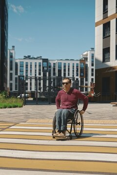 A person using a wheelchair navigates a brightly painted crosswalk in a modern urban area. Surrounding buildings and clear blue sky emphasize the vibrant atmosphere of the day