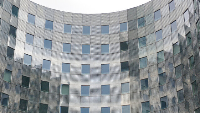 PARIS, FRANCE - SEPTEMBER 1, 2026 - Curved metal facade with square windows reflecting a cloudy sky in La Defense
